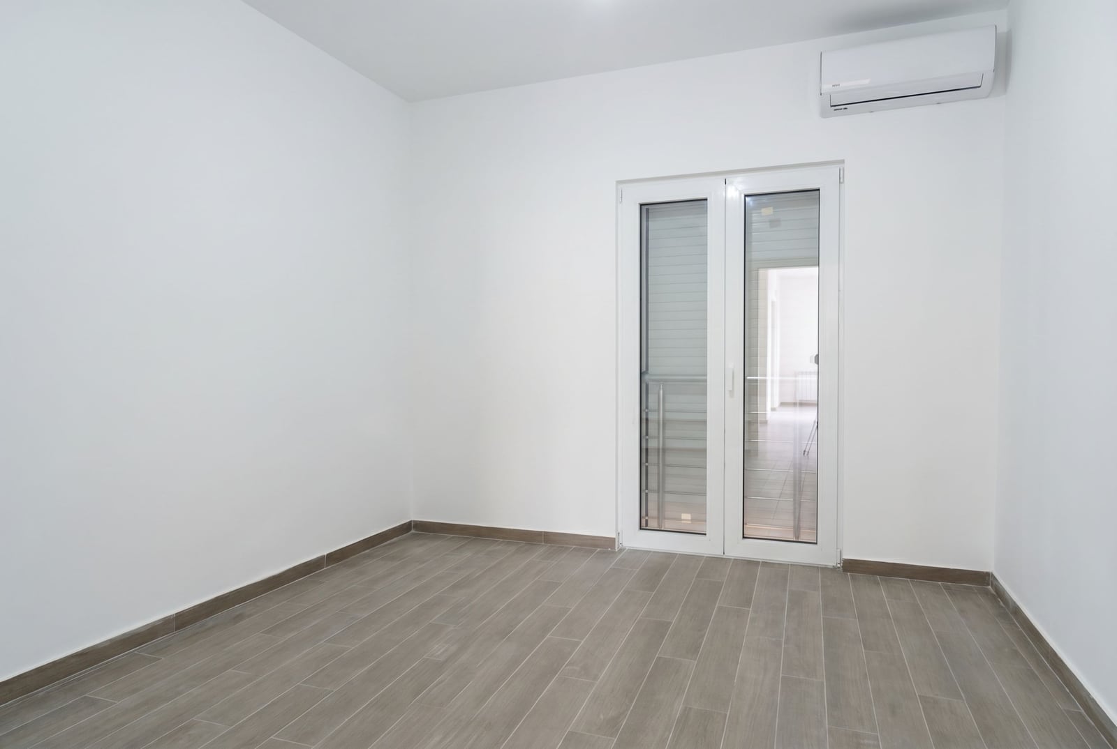 Bright living room in an apartment in Herceg Novi, Montenegro: white walls, wood-look tile flooring, and access to the balcony.
