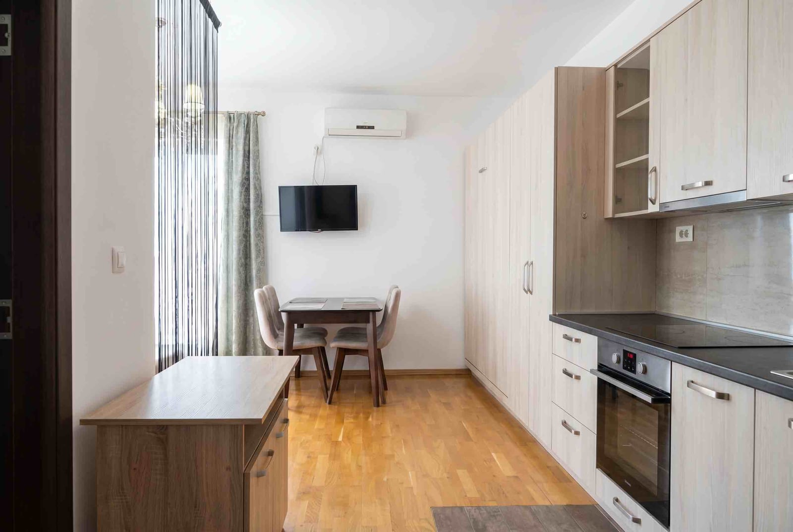 Modern kitchen-living room in an apartment in Budva, Montenegro: light-colored kitchen set, dining area, and built-in appliances.