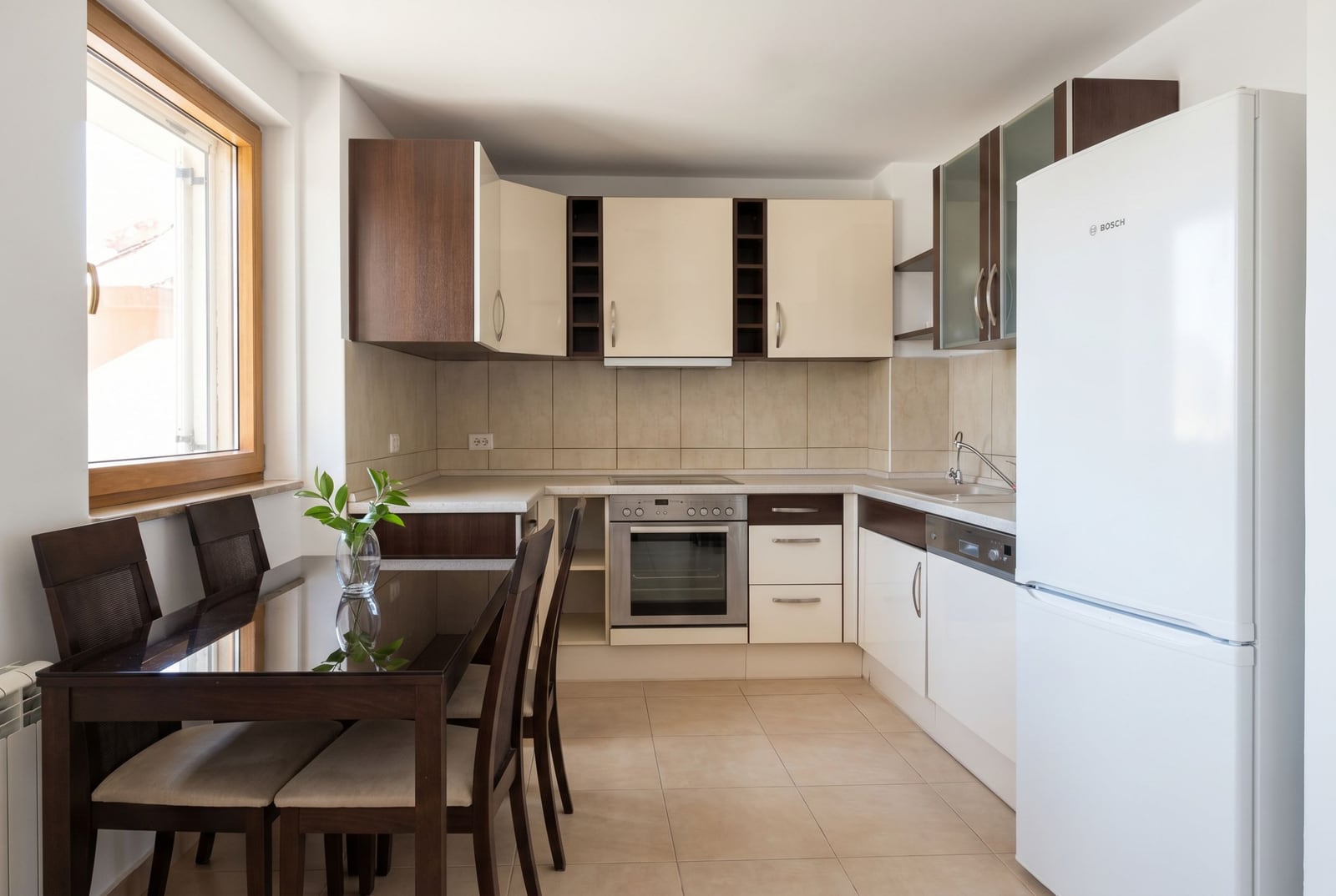 Modern kitchen with dining area in a house, Baošići, Montenegro: built-in Bosch appliances, dark furniture, and light flooring.