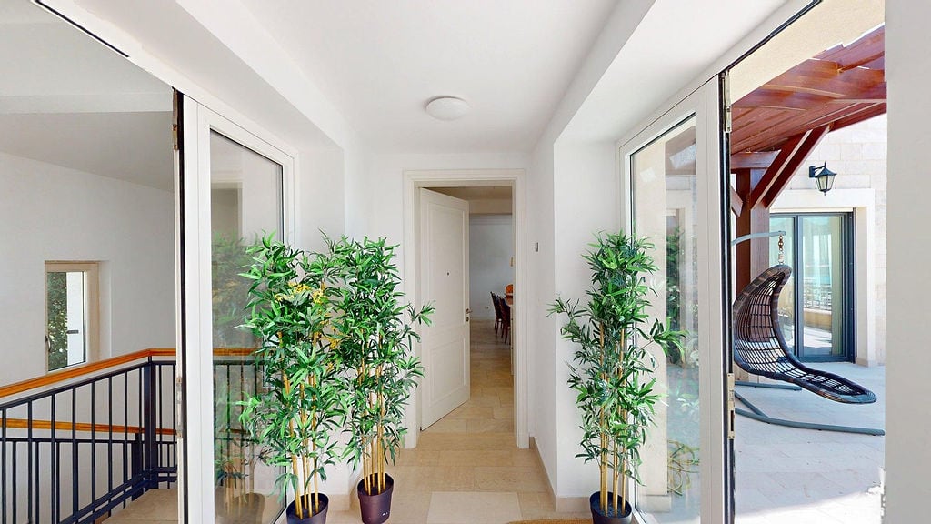 Bright hallway of an apartment in Luštica, Montenegro, with panoramic windows, indoor plants, and access to the terrace.