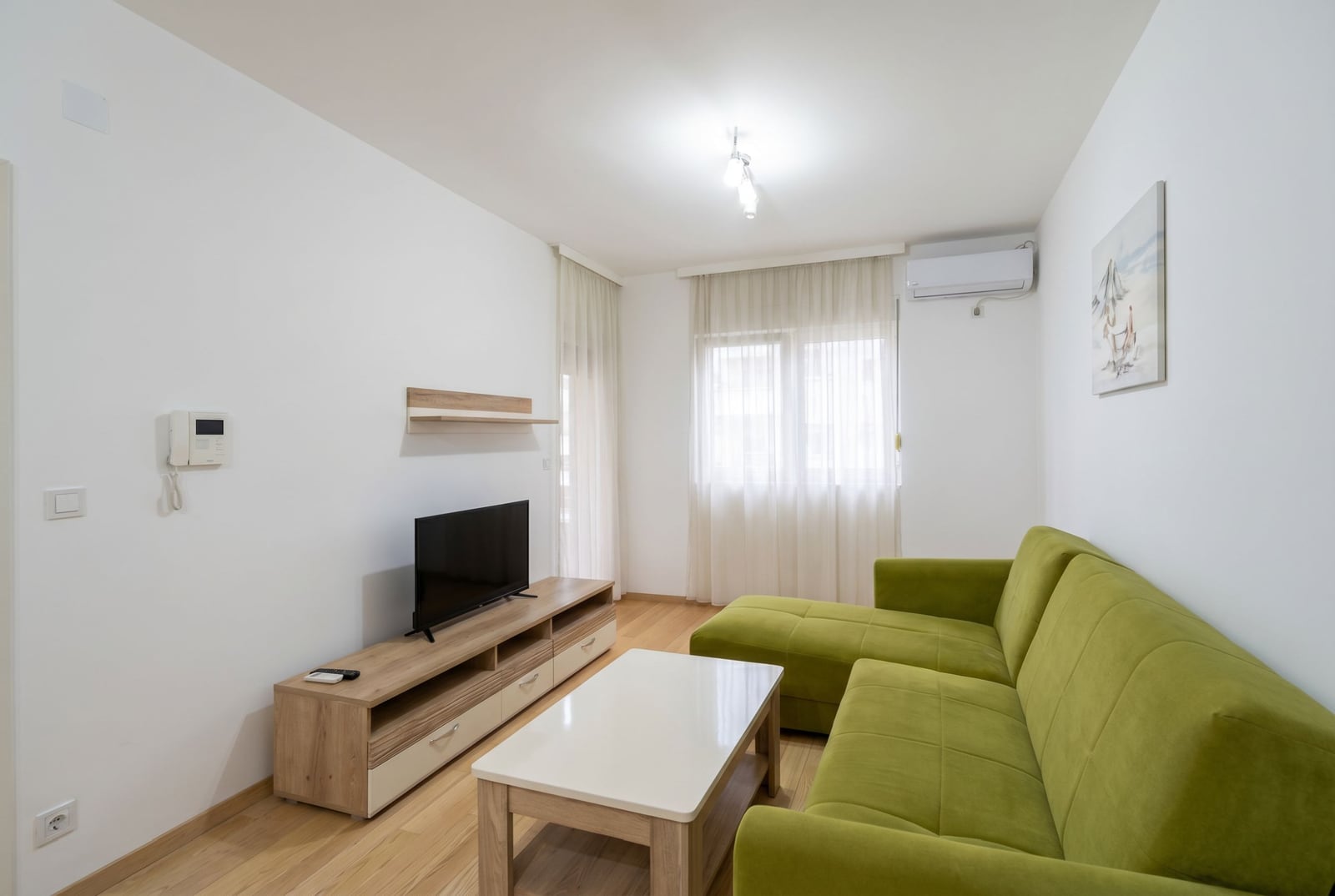 Bright living room in an apartment in Budva, Montenegro: green sofa, TV stand, coffee table, and air conditioner.