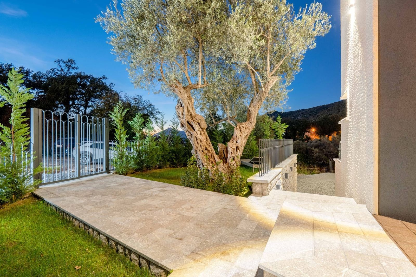 Terrasse de la villa à Kamenovo, Monténégro : revêtement en pierre, vieux olivier, aménagement paysager et vue sur les montagnes au coucher du soleil.