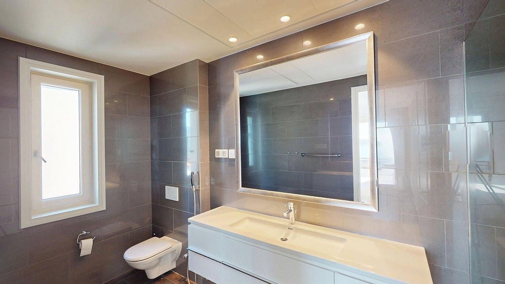 Modern bathroom with gray tiles, a large mirror, and wall-hung fixtures in an apartment, Luštica, Montenegro.