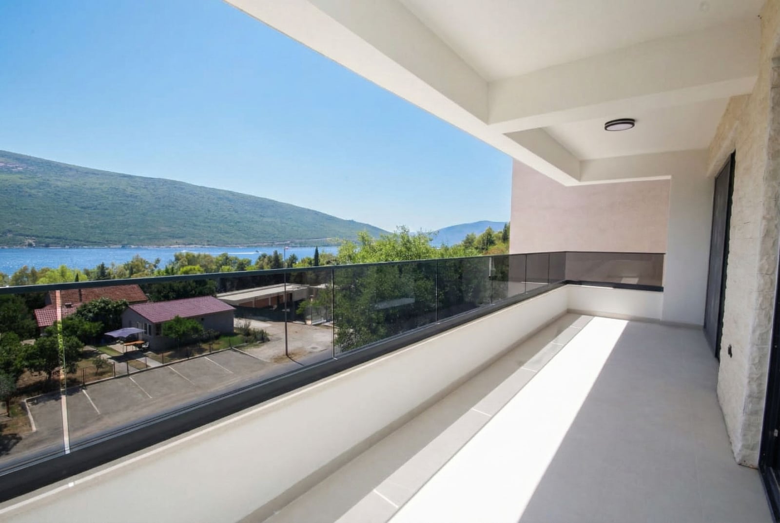 Spacious balcony with panoramic sea and mountain views in an apartment, Kumbor, Montenegro, modern glass railing.