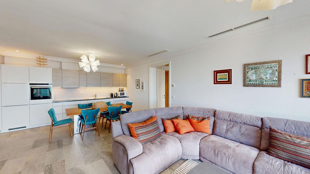 Modern living room with kitchen in an apartment, Luštica, Montenegro: gray corner sofa, dining area, and light interior.