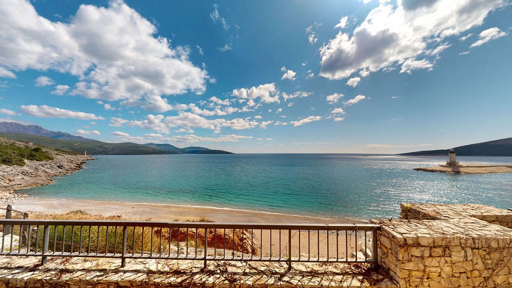 View from the balcony overlooking the sea, beach, and lighthouse in the Luštica residential complex, Montenegro: panoramic seascape and stone finishing.