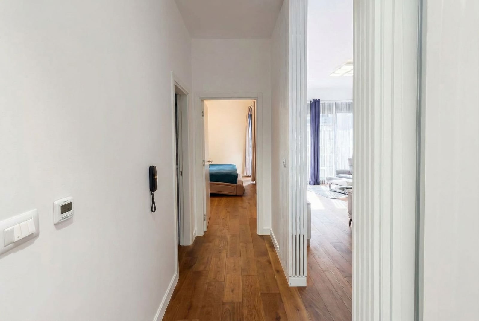 Bright hallway in an apartment in Bar, Montenegro: wooden floor, white walls, and a view of the bedroom and living room.
