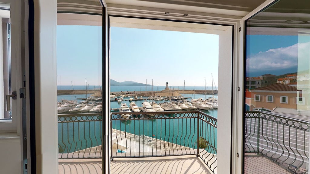 View from the balcony of an apartment in Luštica, Montenegro: a panorama of the yacht marina, pier, and lighthouse on a sunny day.